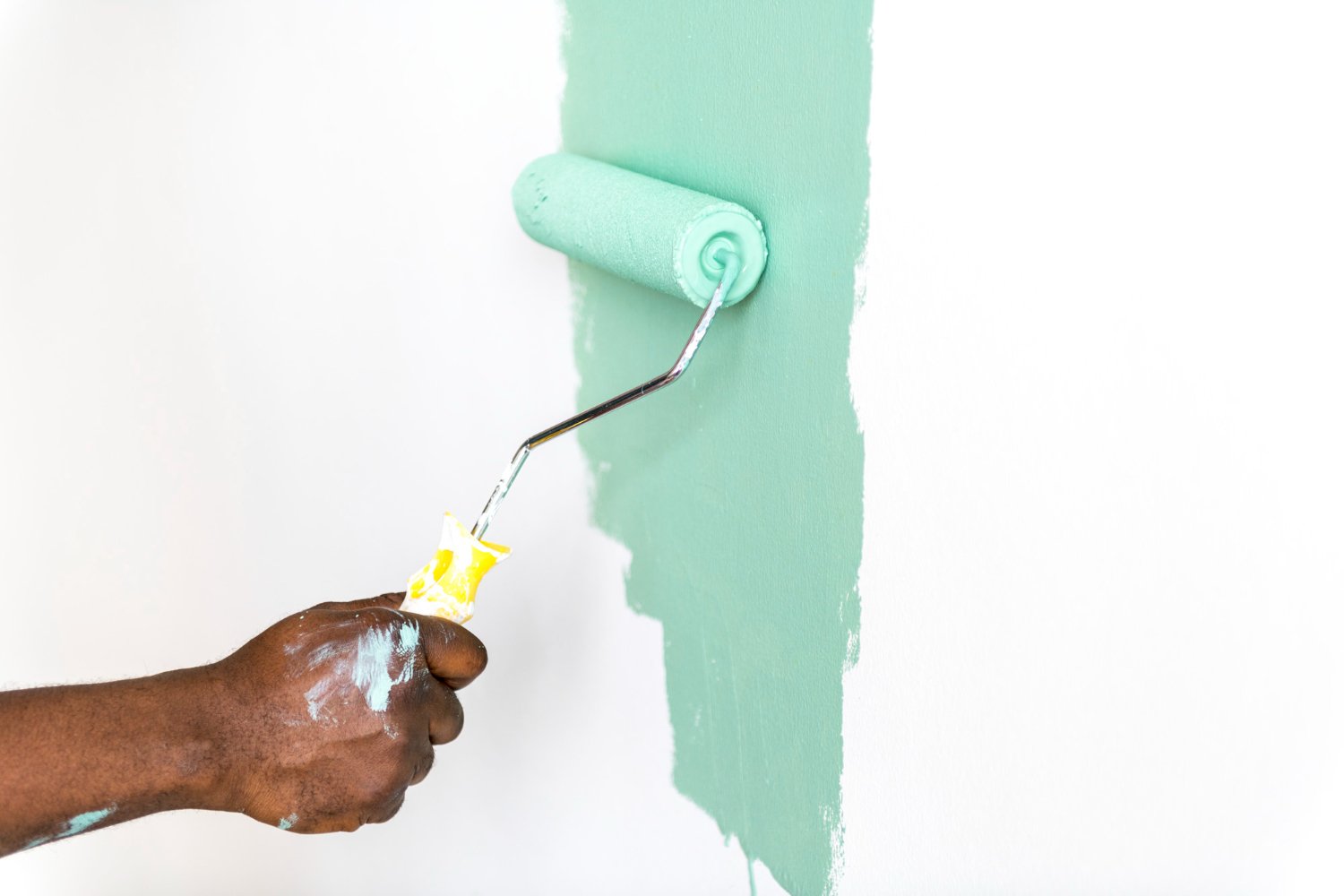 A roller applying pale green paint to a wall